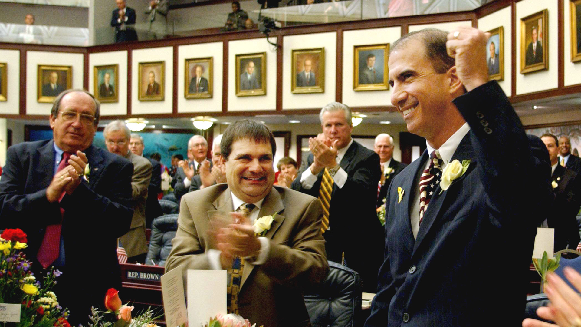 Carey Baker in the Florida legislative chamber raising his fist as colleagues applaud